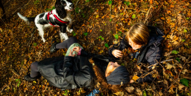 Børn og hund ligger på jorden i en bunke efterårsblade